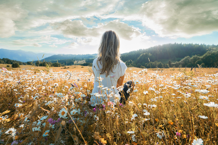 65773448-joven-mujer-sentada-en-el-campo-de-chamomiles-y-mirando-el-cielo-nublado-.jpg